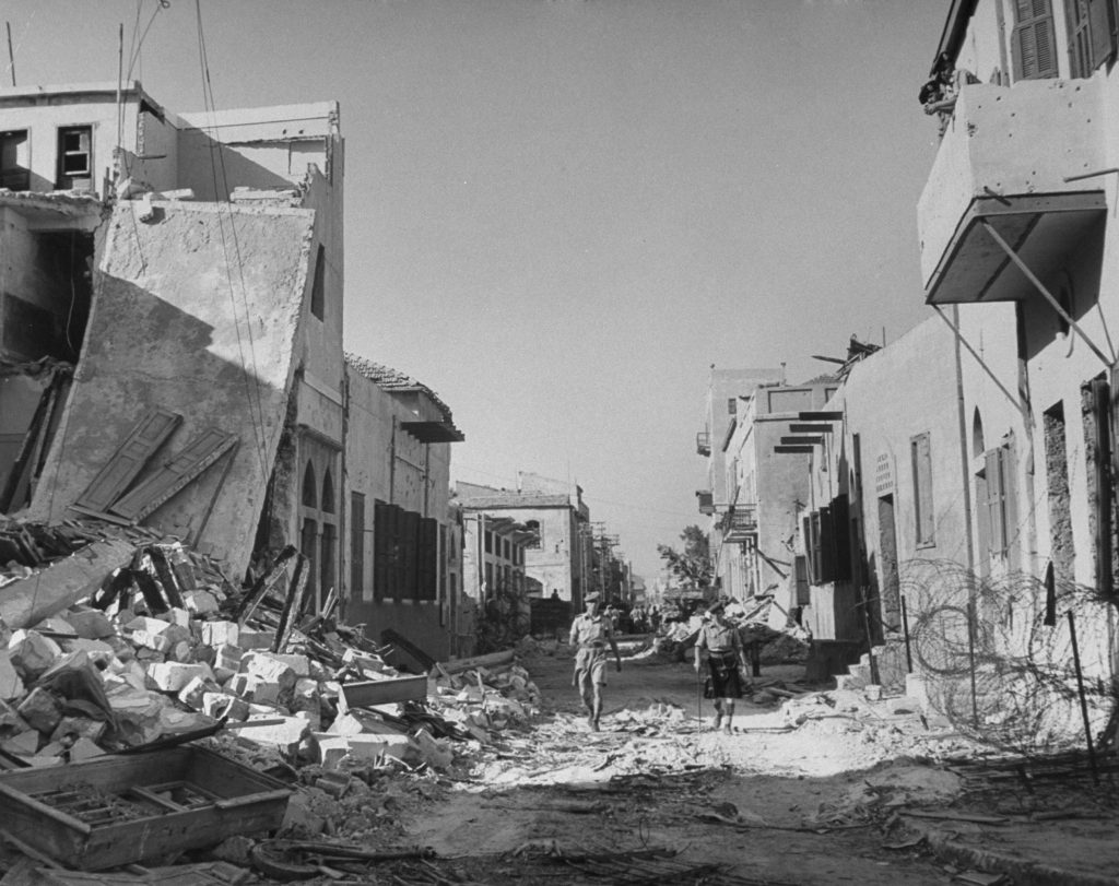 Soldiers walk down a ruined street, shortly after the establishment of the state of Israel, exact location unknown, May 1948.