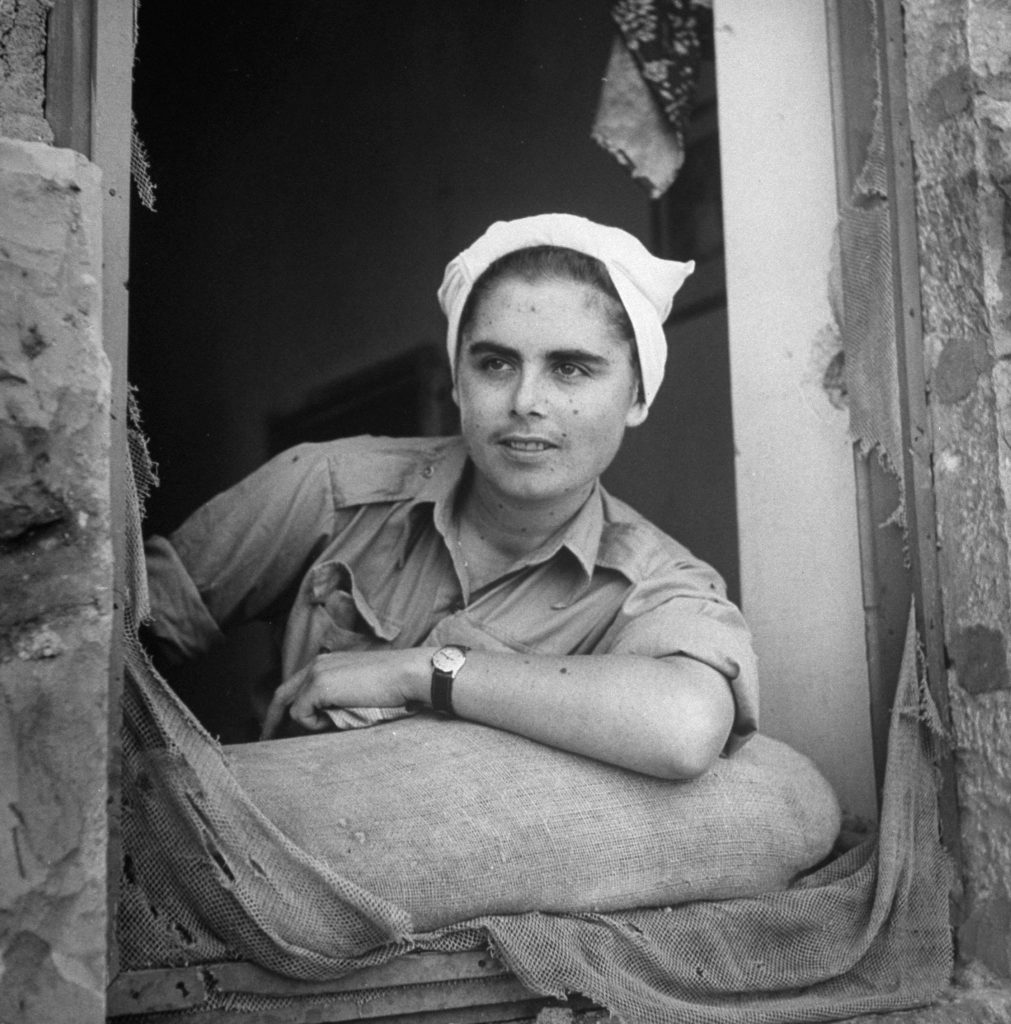 A young woman looks out a battered window shortly after the establishment of the state of Israel, exact location unknown, May 1948.