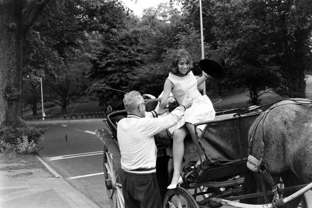 A young woman is helped down from a horse-drawn carriage, Central Park, 1961.