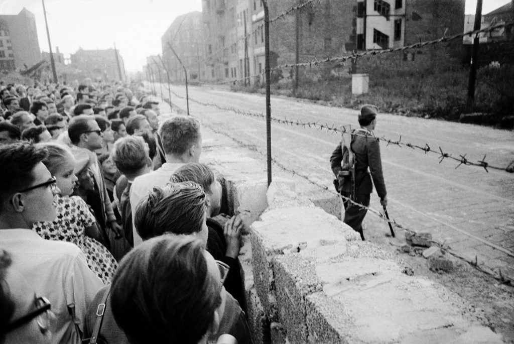 A crowd of West Berlin residents watch as an East German policeman patrols the Berlin Wall.