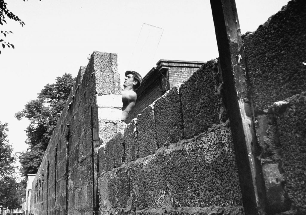 An East German mason builds up a portion of the Berlin Wall